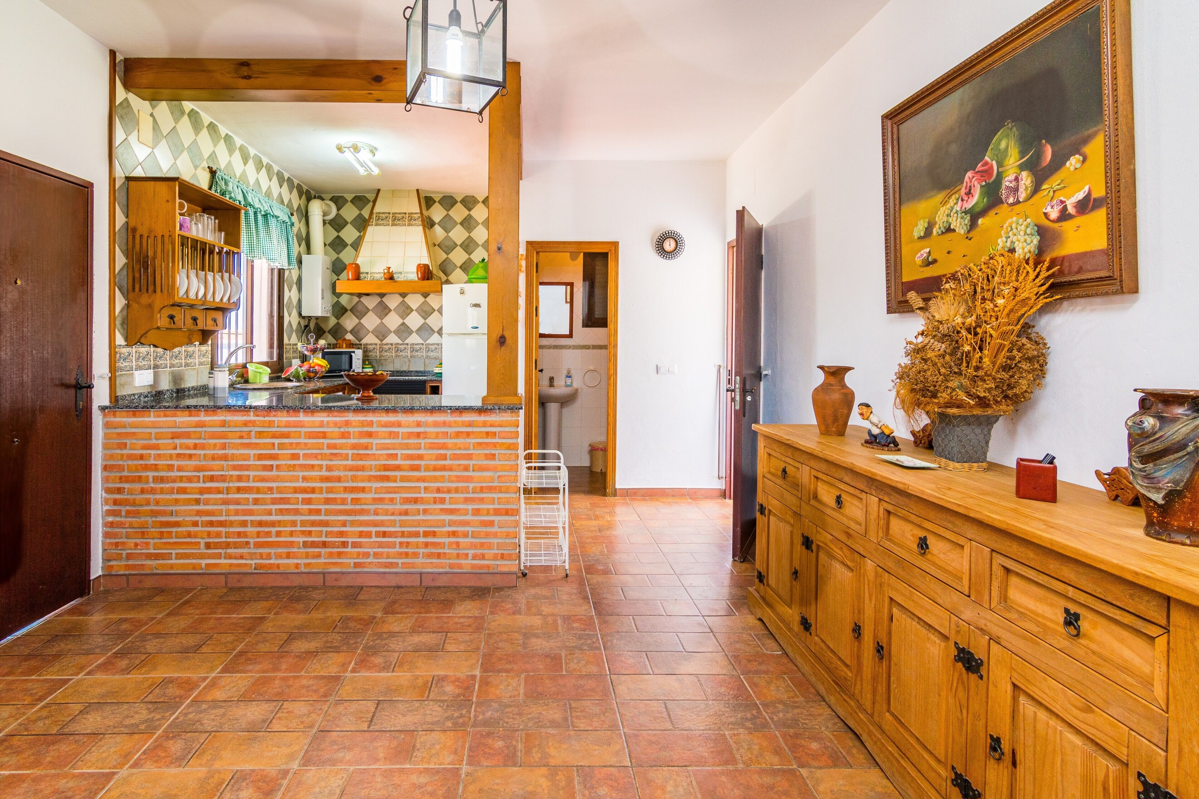 A kitchen with a brick backsplash, wooden cabinets, a tiled floor, and a painting on the wall.
