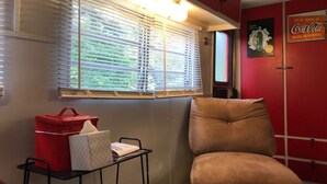 A room with a window, a red wall, a sofa, a small table with a red container, and a poster on the wall. - 1950's Retro experience.  Classic RV.  (SCOTTDALE)