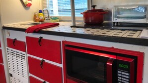 A kitchen with a red microwave, a red pot on the counter, and a window with blinds. - 1950's Retro experience.  Classic RV.  (SCOTTDALE)