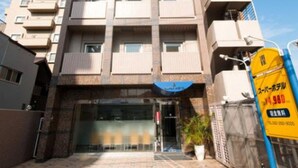 A multi-story building with a central entrance, a blue awning, and a yellow sign with text. - Super Hotel Inn Hakata (Fukuoka)