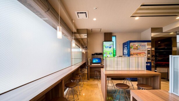 A modern bar area with wooden counters, bar stools, a large screen, and a coffee machine. - Super Hotel Inn Hakata (Fukuoka)