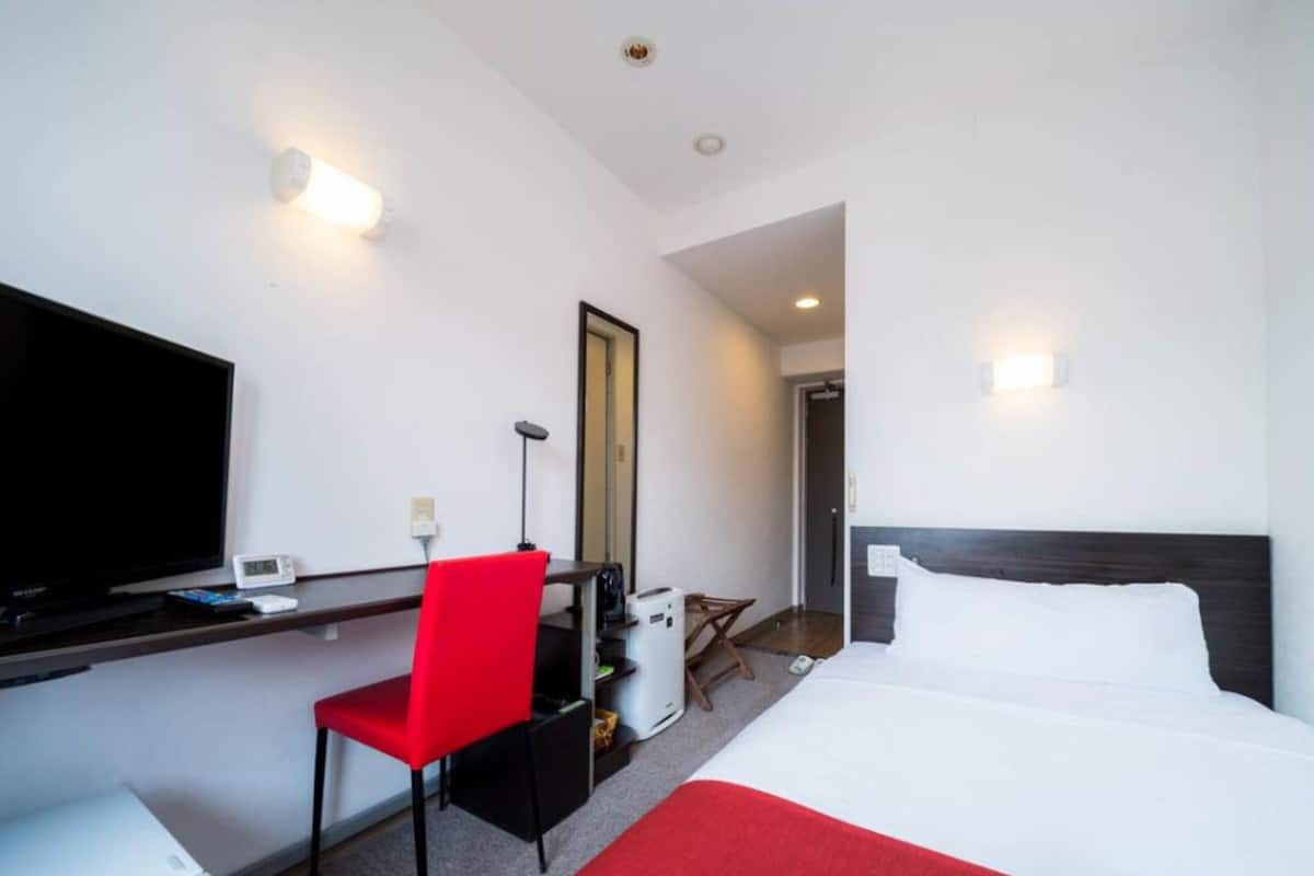 A hotel room with a bed, a desk with a chair, a television, and a mirror.