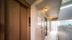 A hallway with wooden doors, a wall-mounted elevator control panel, and a door with a number sign. - Super Hotel Inn Hakata (Fukuoka)