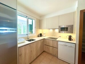 Una cocina moderna con un refrigerador de acero inoxidable, un microondas integrado, un lavavajillas y una ventana con contraventanas.