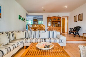 Una sala de estar con un sofá a rayas, una mesa de centro con una cesta, un comedor con sillas y una cocina visible al fondo.