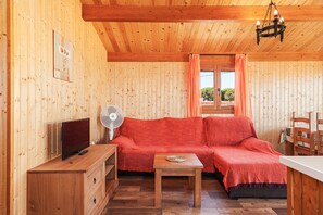 L’intérieur d’un chalet en bois, avec un canapé, une petite table, un téléviseur et un ventilateur.