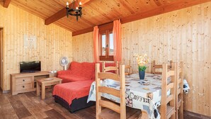 Une pièce en bois avec un lit, une table et des chaises, un téléviseur et un ventilateur.