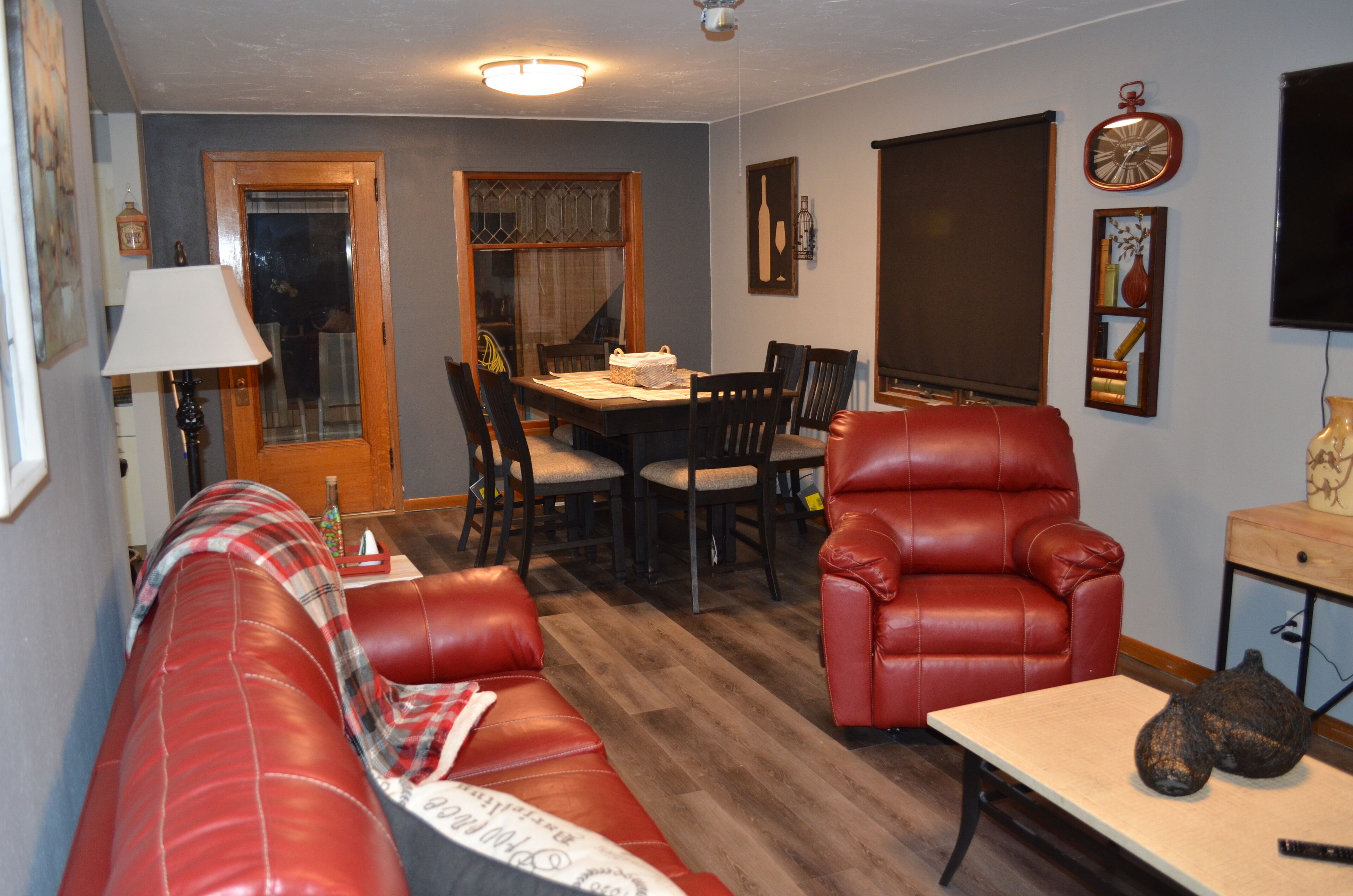 A living room with a red leather sofa, a dining table with chairs, a red armchair, a wooden coffee table, and a wall-mounted clock.
