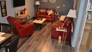 A living room with a red leather sofa, a wooden coffee table, and a TV mounted on the wall. - The Farmhouse...only in town! (Sergeant Bluff)