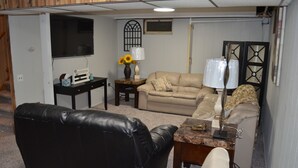 A living room with a black leather couch, beige sofa, and a small coffee table. There is a TV mounted on the wall and a lamp on a side table. - The Farmhouse...only in town! (Sergeant Bluff)