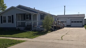A residential street with two houses, one with a porch and a sign for concrete raising, and a garage. - The Farmhouse...only in town! (Sergeant Bluff)