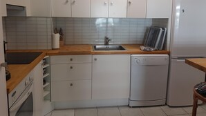 Une cuisine compacte avec des meubles blancs, un plan de travail en bois, un lave-vaisselle encastré et un réfrigérateur.