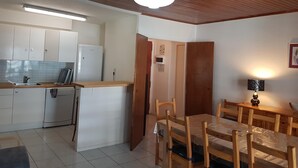 Une cuisine compacte avec des meubles blancs, un réfrigérateur encastré et une table à manger en bois avec des chaises.