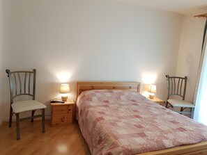 A bedroom with a wooden bed, two nightstands with lamps, and two chairs.