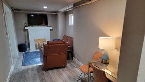 A modern living room with a fireplace, leather chairs, a dining table with chairs, and a TV mounted on the wall.
