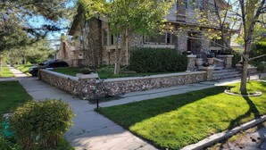 A stone house with a stone staircase, a lawn, and a car parked in the driveway.