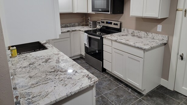 A kitchen with white cabinets, a microwave, a stove, and a sink.
