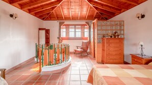 Una camera da letto con soffitto in legno, un letto, una cassettiera, una poltrona a dondolo, una finestra e una scala.
