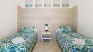 Ein Zimmer mit zwei Betten, einem Nachttisch mit Lampe und einer Ziegelwand.