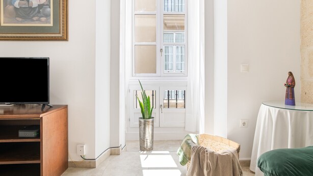 Ein Zimmer mit Fernseher auf einem Holzständer, einer Topfpflanze, einem kleinen Tisch mit einer Statue und einer Tür mit Fenster.