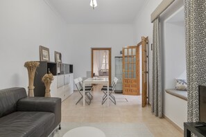 A modern living room with a sofa, a dining table with chairs, a television, and a kitchen area with cabinets.
