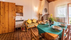 A cozy room with a wooden ceiling, a dining table set with plates and glasses, a sofa with yellow cushions, and a view through a window. - Cozy Apartment with Balcony, Lake View & Wi-Fi; Parking Available, Pets Welcome (San Zeno di Montagna)