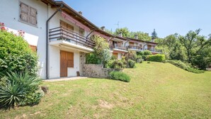 A row of two-story houses with balconies, surrounded by greenery and a sloped lawn. - Cozy Apartment with Balcony, Lake View & Wi-Fi; Parking Available, Pets Welcome (San Zeno di Montagna)