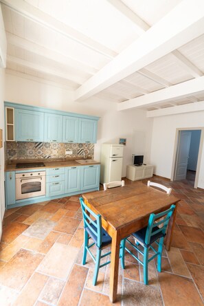 Cozinha com armários azuis, uma mesa de madeira e cadeiras, e piso ladrilhado.