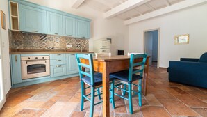 A kitchen with teal cabinets, a wooden dining table, and chairs, a refrigerator, and a tiled floor. - Apartment 'Il Rosmarino' with Sea View, Wi-Fi and Air Conditioning (Patresi)