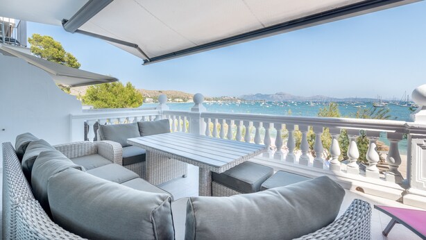 A balcony with wicker furniture, a table, and a view of the sea and boats.