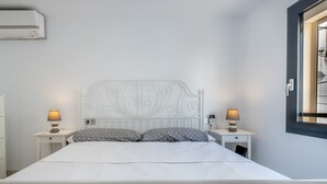 A neatly made bed with a white headboard, two bedside tables with lamps, and a window with blinds.