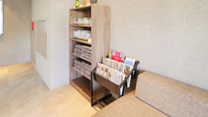 A hotel reception area with a wooden reception desk, a shelf with magazines and a bottle, and a door with a fire alarm. - Odawara Terminal Hotel (Odawara)