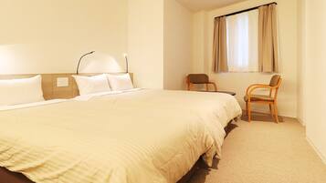Habitación de hotel con una cama grande, dos sillas, una ventana con cortinas y una lámpara fijada a la pared.