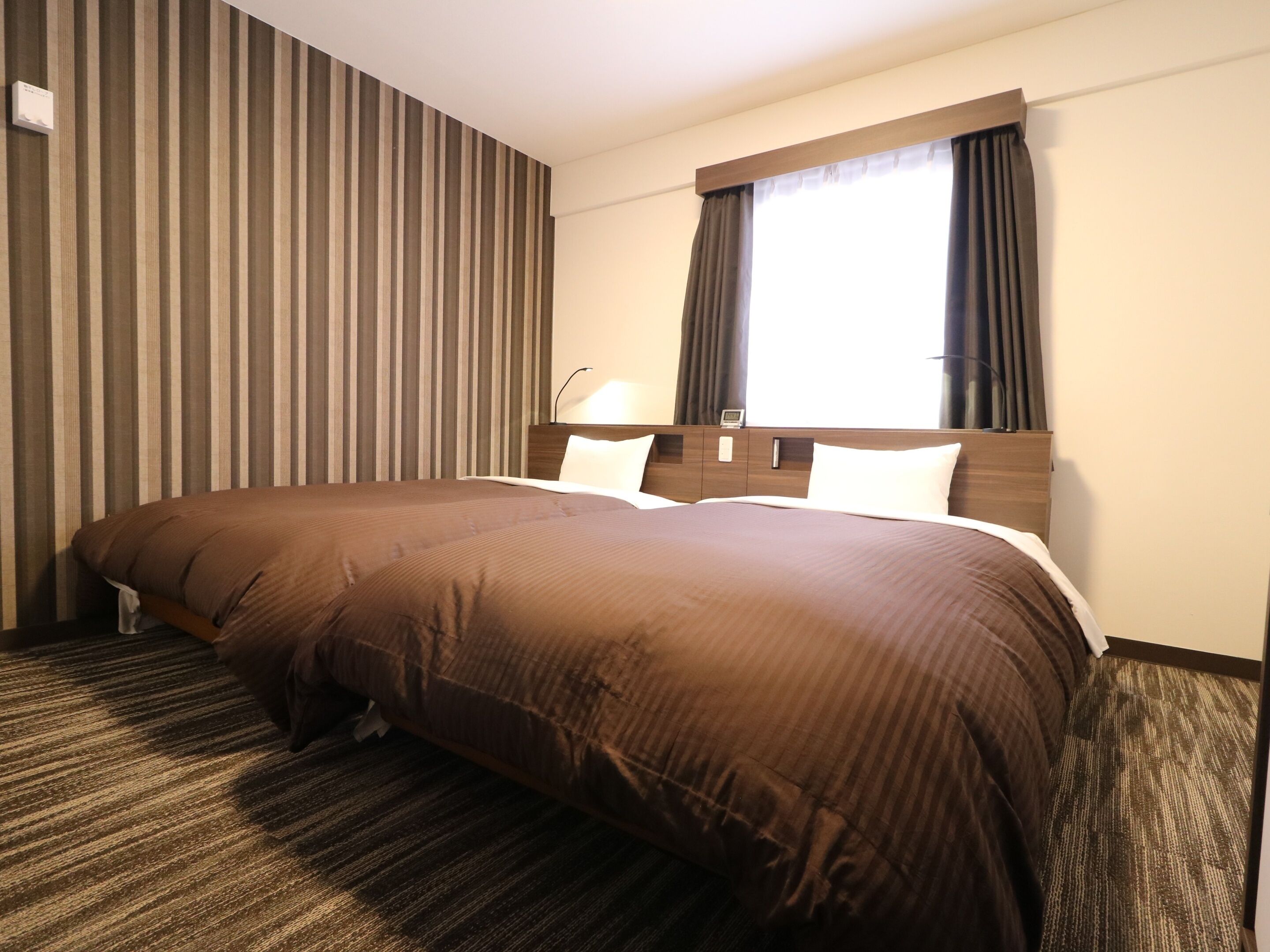 A hotel room with a large bed, a bedside table, a lamp, and a window with curtains.