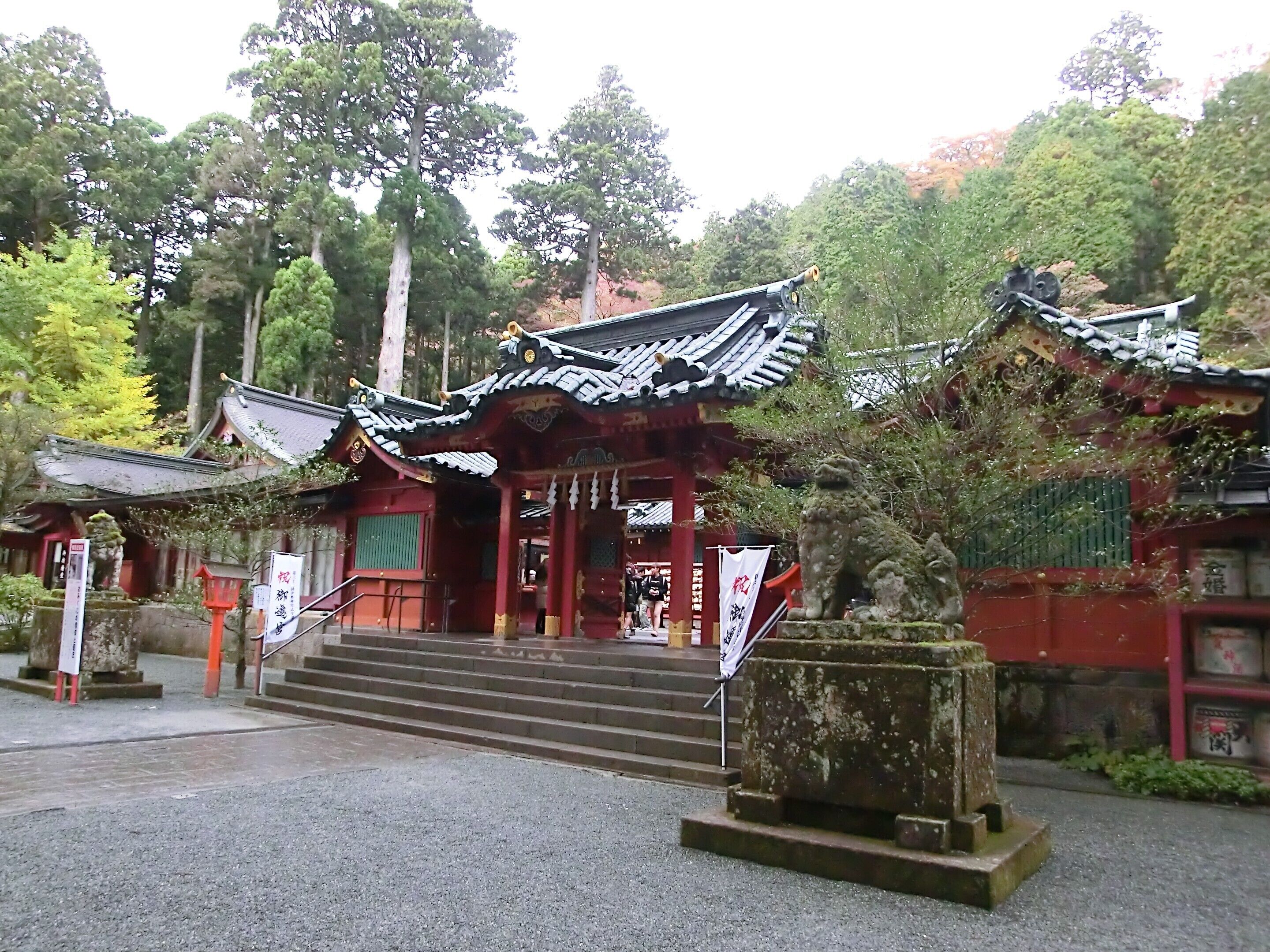 A traditional Japanese temple with a red building, a stone lion statue, and a staircase leading to the entrance.