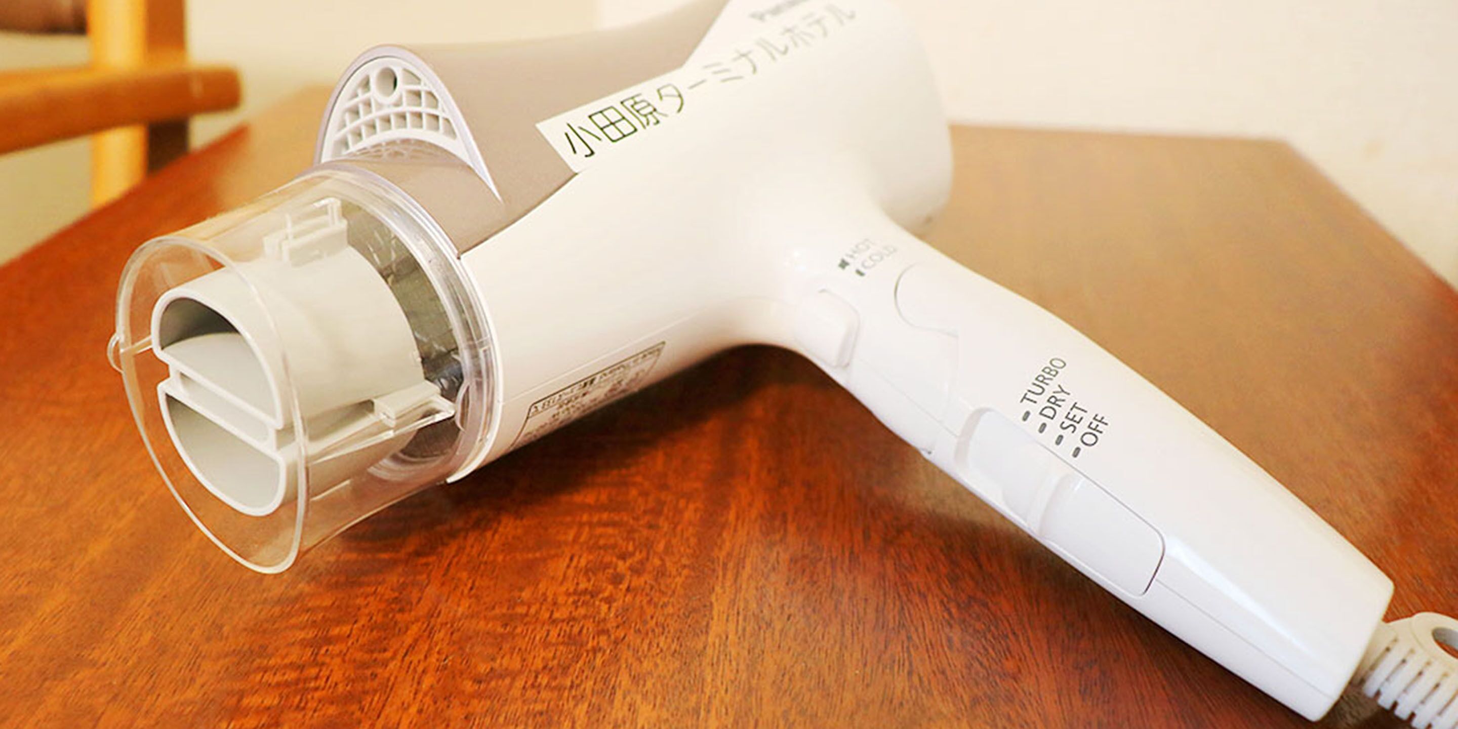 A white hair dryer with Japanese text on it, lying on a wooden surface.