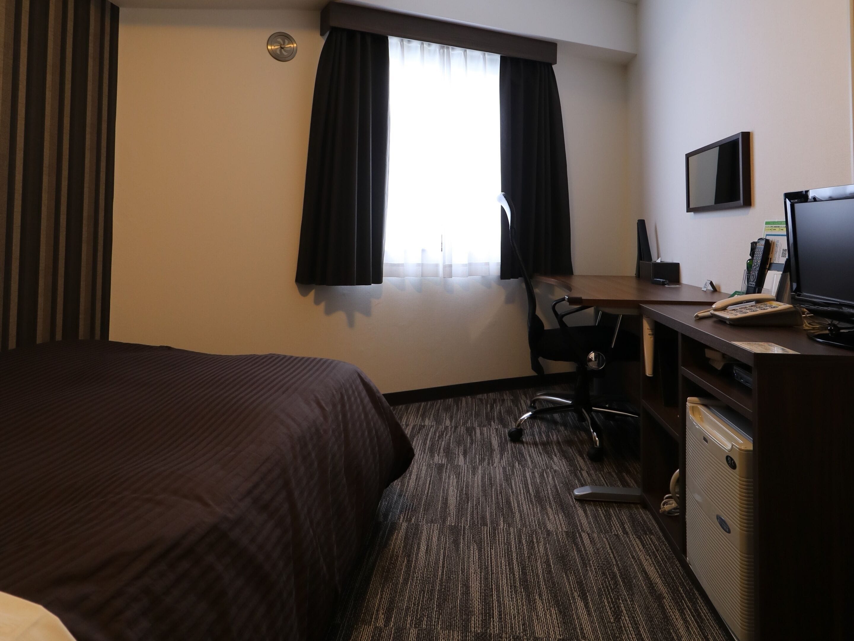 Ett hotellrum med en säng, ett skrivbord med en dator, en telefon och en tv.
