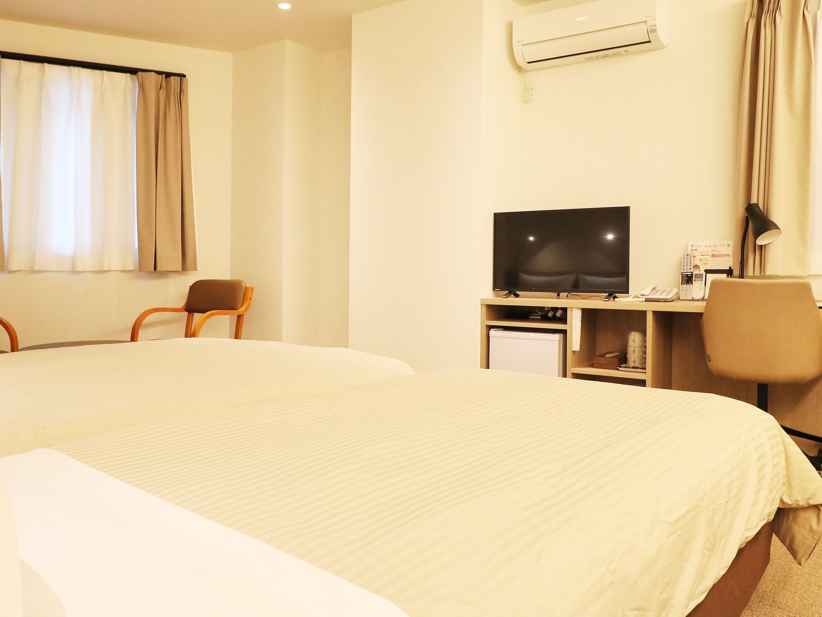 A hotel room with a large bed, a desk with a television, a chair, and a small refrigerator.
