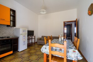 Une cuisine compacte équipée d’un réfrigérateur, d’une cuisinière et de meubles de rangement orange. Une table à manger, entourée de chaises, est placée au centre de la pièce.