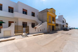 Une rue côtière bordée de bâtiments blancs, avec un bâtiment jaune à l’angle et des voitures garées.