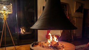 Un salon moderne doté d’un poêle à bois central, d’un lampadaire et d’une porte en verre donnant sur une autre pièce.