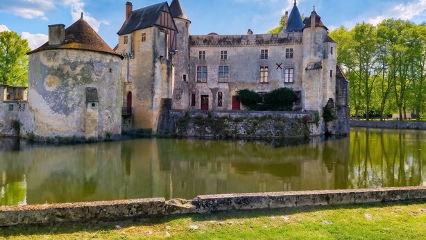 Un château historique, doté d’un fossé, de murs en pierre et situé en bord de rivière.