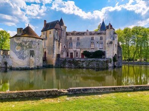 Un castillo histórico con un foso, muros de piedra y un río frente a él.