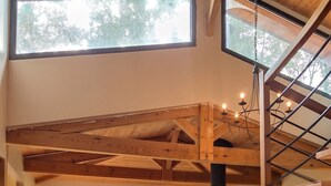 Un vaste espace de vie doté d’un haut plafond, de poutres en bois, d’une table à manger avec des chaises, d’un canapé et d’une grande fenêtre donnant sur un jardin.