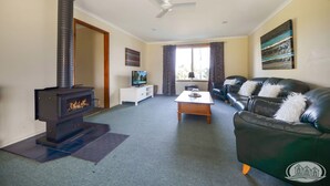 A living room with a fireplace, a sofa, a coffee table, a TV, and a ceiling fan. - A quiet retreat just a stroll from the ocean (Allestree)