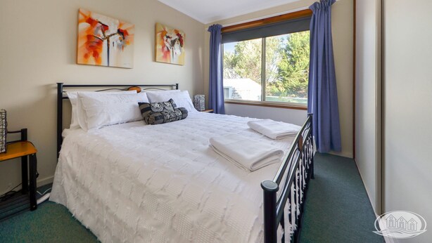 A neatly made bed with white linens, a bedside table with a lamp, and two paintings on the wall. - A quiet retreat just a stroll from the ocean (Allestree)