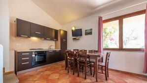 A kitchen with dark cabinets, a dining table with chairs, a TV mounted on the wall, and a window with curtains. - Holiday home on the sea, immersed in nature – Accu is Prezzus E special (Villasimius)