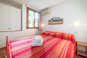 Une chambre à coucher avec un lit, une fenêtre, un appareil de climatisation, un tableau et une table de chevet.