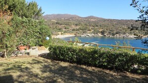 A coastal landscape with a clear view of the sea, a wooden deck, and surrounding greenery. - Sea View House Near the Beach – Casa Accu is Prezzus F (Villasimius)