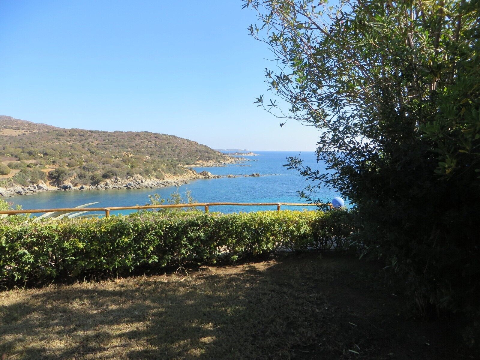 Un paisaje costero con vistas claras al mar, una cerca de madera y una colina al fondo.